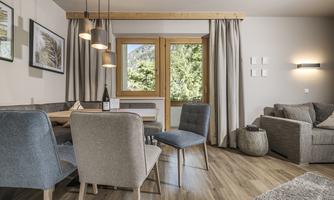A cozy living space with a dining table and chairs. Large windows let in plenty of daylight and provide a view of the outdoors.