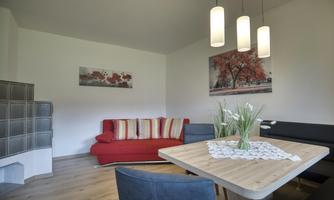 A modern living room with a red sofa and light walls. The table is decorated with a tablecloth and stylish lamps hang from the ceiling.