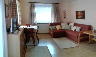 A cozy living room with a red sofa and a table. Large windows provide plenty of daylight and a welcoming atmosphere.