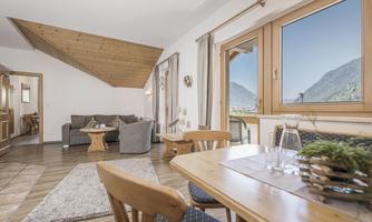 A cozy living room with wood paneling and large windows that offer a view of the mountains. A dining area with wooden chairs and a table complements the space.