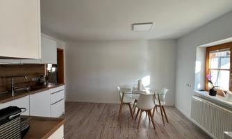A modern, bright kitchen and dining area with a table and chairs. The walls are in a neutral tone and there is plenty of natural light.