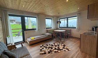 A cozy living and dining room in a holiday apartment. Large windows offer a view of the surrounding landscape.