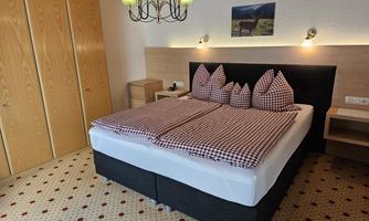 A cozy bedroom with a large bed and checkered bedcovers. In the background, there is a wardrobe and a picture on the wall.