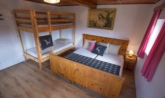 A cozy bedroom with a double bed and a bunk bed. The walls are painted light, and there is a beautiful mural as well as decorative cushions.
