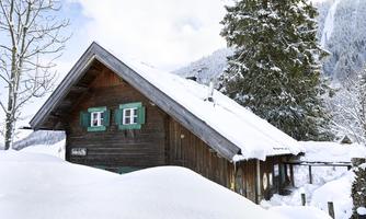 A charming wooden house amidst a snowy landscape. The windows are green and the snow lies high around the house.