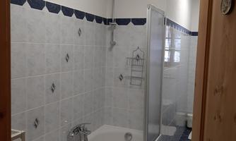 A modern bathroom with a bathtub and a shower. The walls are light tiled and the lighting is friendly.