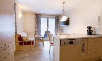 A modern kitchen with wooden cabinets and a small dining area. The room is bright and inviting, with a view of a balcony.