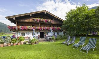 A traditional alpine house with colorful flowers on the balcony. In the foreground, there are deck chairs on a green meadow.