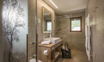 A modern bathroom with a large shower and a wooden washbasin. Natural light filters through the window and a decorative glass wall features a tree-like motif.