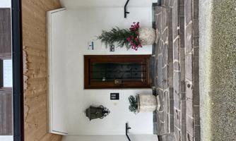An entrance with a wooden porch and a beautiful door. Next to the door are two flower pots with flowers.