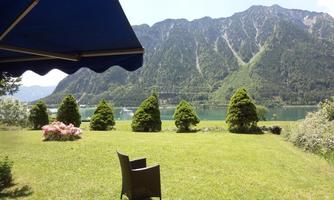 A picturesque landscape with green grass, a comfortable seating area, and mountains in the background. The view of the calm lake complements the peaceful atmosphere.