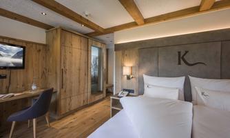 A modern hotel room with wooden furniture and a cozy double bed. The warm lighting and the television add an inviting touch to the atmosphere.