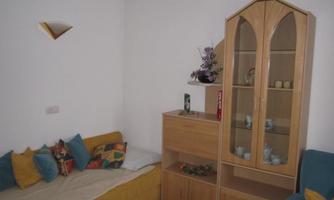 A cozy living room with a sofa and colorful cushions. In the background, there is a wooden shelf with decorations and dishes.
