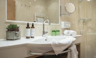 A modern bathroom with a sink, toiletries, and fresh towels. There is also a mirror and a shower in the background.