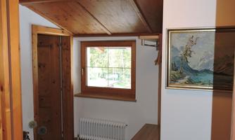 A bright hallway with wood paneling and a large window. There is a picture hanging on the wall, and there is a small cabinet.
