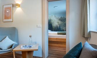 A cozy living space with a comfortable armchair and a small table. Through the open door, a room with a pleasant forest motif can be seen.