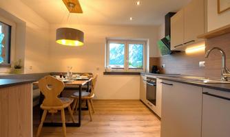 A modern kitchen with wood and gray elements. There is a dining table with chairs and many windows that let in light.