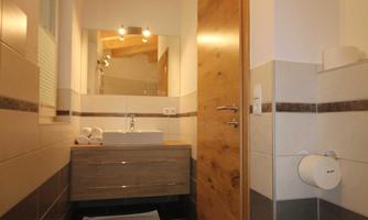 A modern bathroom with a wooden ceiling and large tiles. There is a sink, a mirror, and a toilet.