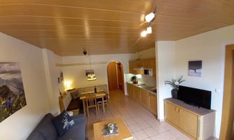 A bright apartment with a wooden ceiling and modern furniture. There is a kitchen, a dining area, and a cozy living room.