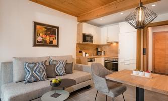 A modern living room with a cozy couch and a dining table. The kitchen is modernly equipped, and the walls are in neutral colors.