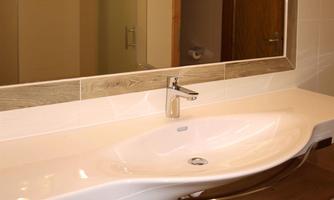 A modern bathroom with a large, curved sink and a mirror. There are towels on a wooden shelf and access to a shower in the background.