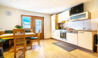 A modern kitchen with wooden furniture and a large table. There is plenty of natural light and an inviting atmosphere.