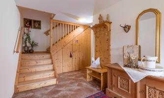 An inviting hallway with a wooden staircase and decorative details. In the background, there are plants and a traditional piece of furniture.