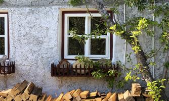 A charming house with white walls and two windows. In front of the house lies a stack of firewood.