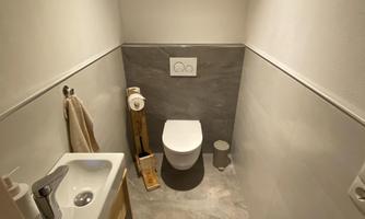 A modern bathroom with a toilet and a sink. The walls are light, and the floor is designed with gray tiles.