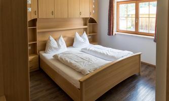 A cozy bedroom with a wooden bed and two pillows. The warm colors and natural light create an inviting atmosphere.