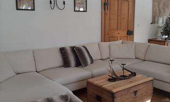 A modern living room with a beige sofa and a wooden trunk table. Two frames hang on the walls, and there is a wood-glass door.