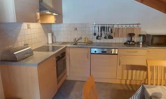 A compact kitchen with a wooden ceiling, equipped with modern appliances. A dining table and chairs invite you to linger.
