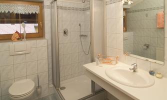 A bright bathroom with a shower, a sink, and a toilet. The walls are tiled and the room is well-lit.