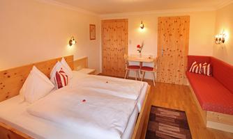 A cozy bedroom with two beds and modern wooden decor. The room features a small dining area and a comfortable seating corner.