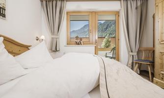 A cozy room with a large bed and a view of the mountains. The windows are decorated with curtains and there is a sitting area.