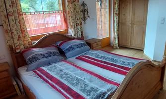 A cozy bedroom with a large wooden bed and colorful pillows.  
Windows with curtains and a wooden wardrobe complete the room.