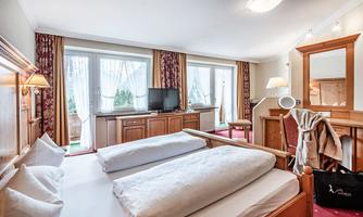 A cozy hotel room with two single beds and a wooden furniture design. Large windows allow for plenty of daylight and provide a relaxing atmosphere.