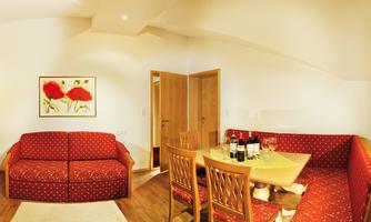 A cozy living space with red sofas and a wooden table. In the background, flower pictures hang on the wall.