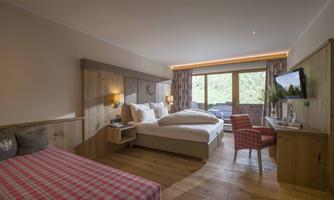 A modern hotel room with a large bed and a small single bed. The furniture is made of wood and there is a balcony overlooking nature.