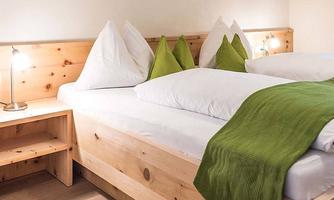 A cozy bedroom with a wooden double bed and green cushions. The soft lighting creates a relaxed atmosphere.