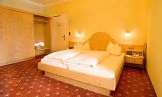 A cozy hotel room with a large bed and a warm yellow wall color. There is a wardrobe and soft lighting for a relaxed atmosphere.