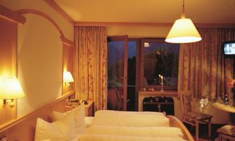 A cozy hotel room with two beds, soft lighting, and a balcony. The space is tastefully furnished and exudes a relaxed atmosphere.