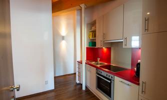 A modern kitchen with red accents and a wooden ceiling. It features a stove, an oven, and practical storage options.