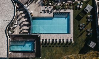 An elegant outdoor pool with loungers and a green lawn. In the background, a smaller pool is visible.