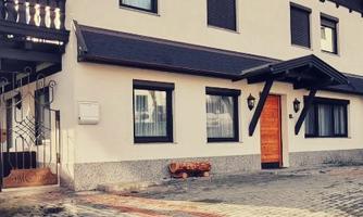 A modern house with a light facade color and wooden details. The entrance is marked by a solid wooden door and the floor is made of square paving stones.