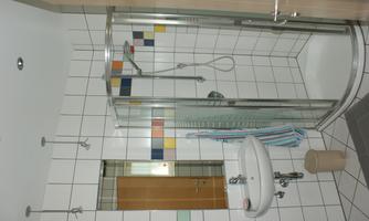A modern bathroom with a glass shower and a sink. The walls are decorated with white tiles and colorful accents.