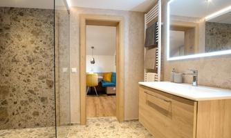 A modern bathroom with a wooden washbasin and a large mirror. In the background, you can see a cozy living area with colorful chairs.