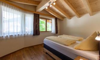 A bright bedroom with wooden ceilings and large windows. The room is furnished with a double bed and a nightstand.