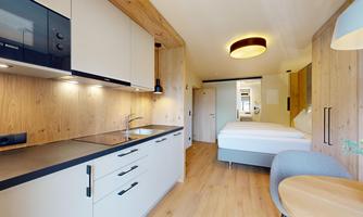 A modern and cozy apartment with a fully equipped kitchenette and a bedroom. The wood paneling creates a warm atmosphere.