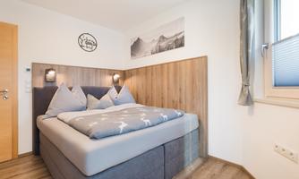 A modern bedroom with a comfortable bed and wood paneling. Brightly lit, with a large window and tasteful decoration.
